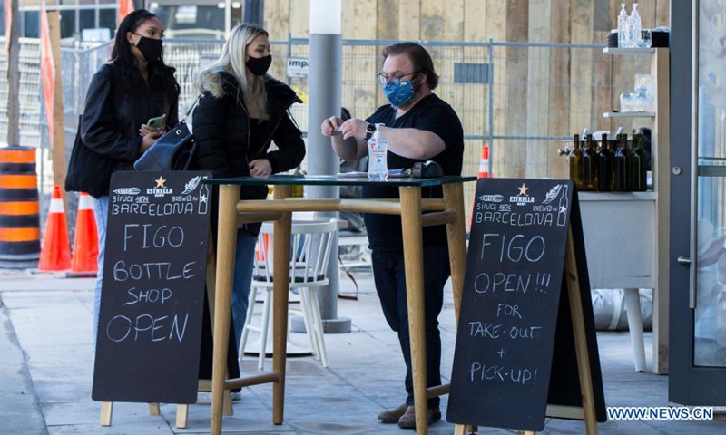 A waiter wearing a face mask sets a table for customers at the outdoor area of a restaurant in Toronto, Canada, on March 20, 2021. With distancing rules and a number of other public health and workplace safety measures, outdoor dining was allowed to resume Saturday in Toronto under modifications to the Ontario's color-coded pandemic response framework. (Photo by Zou Zheng/Xinhua)