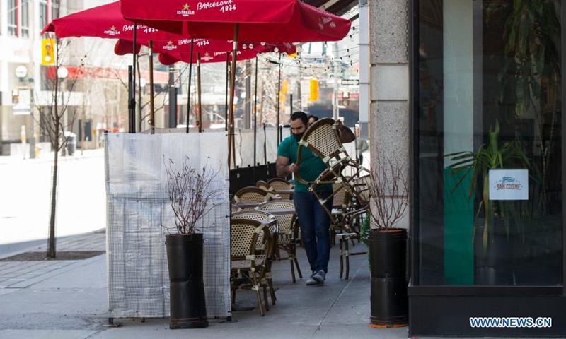 A waiter wearing a face mask prepares chairs for customers at the outdoor area of a restaurant in Toronto, Canada, on March 20, 2021. With distancing rules and a number of other public health and workplace safety measures, outdoor dining was allowed to resume Saturday in Toronto under modifications to the Ontario's color-coded pandemic response framework. (Photo by Zou Zheng/Xinhua)
