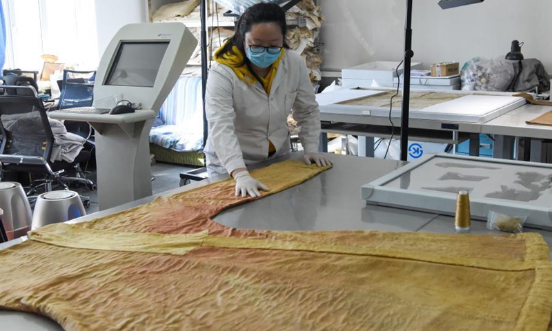 A staff arranges a restored silk robe at the Museum of Xinjiang Uygur Autonomous Region in Urumqi, northwest China's Xinjang Uygur Autonomous Region, March 19, 2021. Northwest China's Xinjiang Uygur Autonomous Region has restored 118 prominent antique items under five restoration projects lasting three years.(Photo:Xinhua)