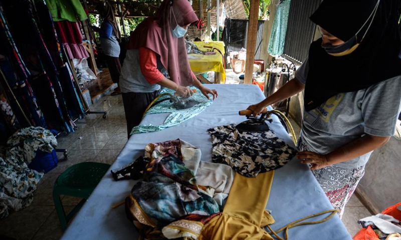 Workers wearing face mask iron finished clothes at the NCK Textile home factory at Curug village in Bogor, West Java, Indonesia, on March 23, 2021. NCK Textile produces clothes to orders from local markets, and provides job opportunities to people in its neighborhood.(Photo: Xinhua)