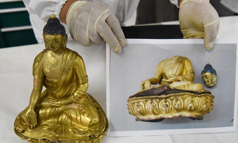 A staff shows a restored gold-plated bronze Buddha statue next to a photo showing the statue before restoration at the Museum of Xinjiang Uygur Autonomous Region in Urumqi, northwest China's Xinjang Uygur Autonomous Region, March 19, 2021. (Xinhua)