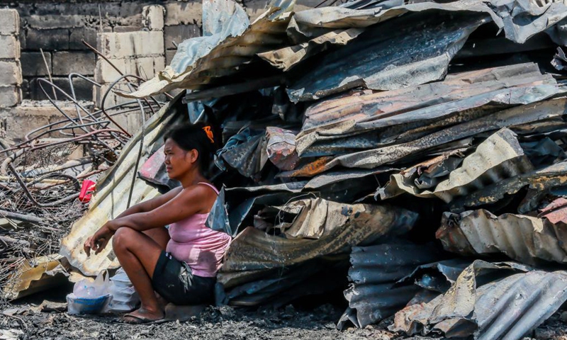 A woman rests under the shade of recovered metal roofs from their charred home after a fire at a slum area in Rizal Province, the Philippines on March 26, 2021. The Philippine Bureau of Fire Protection said that the fire is believed to have started from one of the houses that was being used as a garment manufacturing area, leaving more than 170 families homeless in the fire.Photo:Xinhua