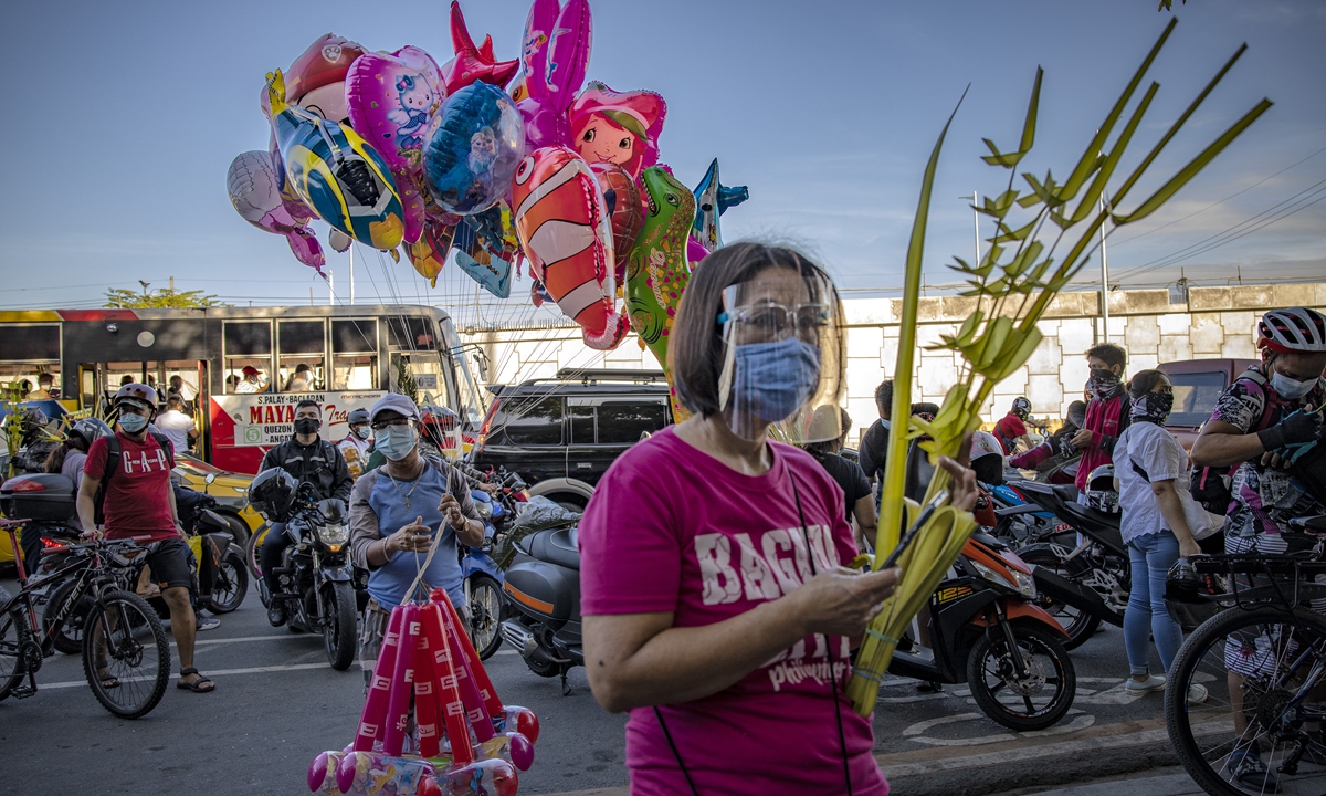 A woman wearing a face mask and face shield carries a palm frond as she prays outside a church to celebrate Palm Sunday in Quezon City, Metro Manila, the Philippines, on Sunday. Catholics are gathering to celebrate Palm Sunday even as authorities have prohibited religious gatherings as part of measures to curb the spread of COVID-19. Photo: VCG
