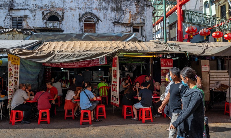 People wearing face masks walk past a food stall in Kuala Lumpur, Malaysia, March 28, 2021.(Photo: Xinhua)