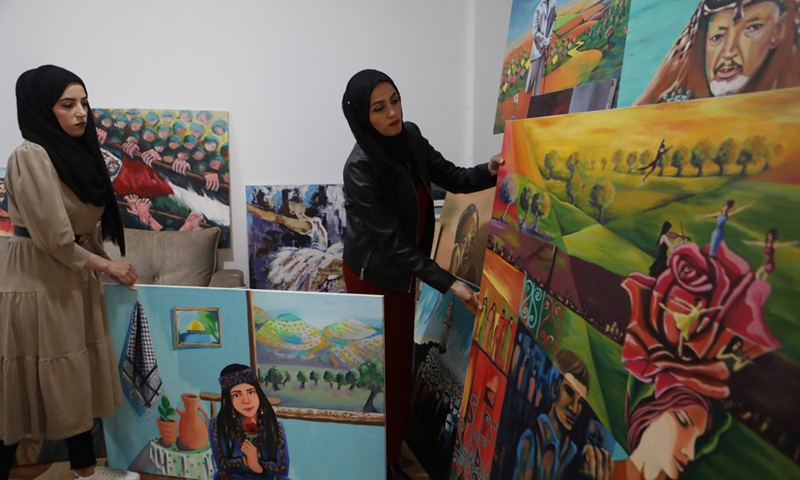 Palestinian sisters Samia al-Masri (R) and Doaa al-Masri display their paintings at their home in the al-Fawwar refugee camp, south of West Bank city Hebron, April 3, 2021.(Photo: Xinhua)