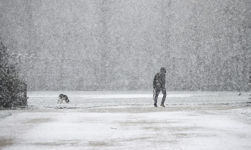 A person walks a dog amid snow at the Park of the Fiftieth Anniversary in Brussels, Belgium, April 6, 2021.(Photo: Xinhua)