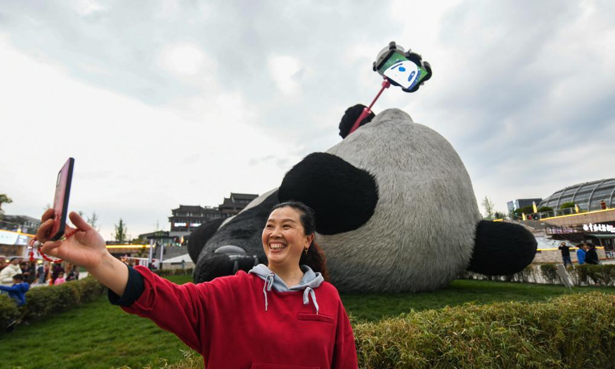 A tourist poses for a selfie with the Selfie Panda sculpture at Yangtianwo square in Dujiangyan, southwest China's Sichuan Province, April 7, 2021. (Xinhua/Wang Xi)