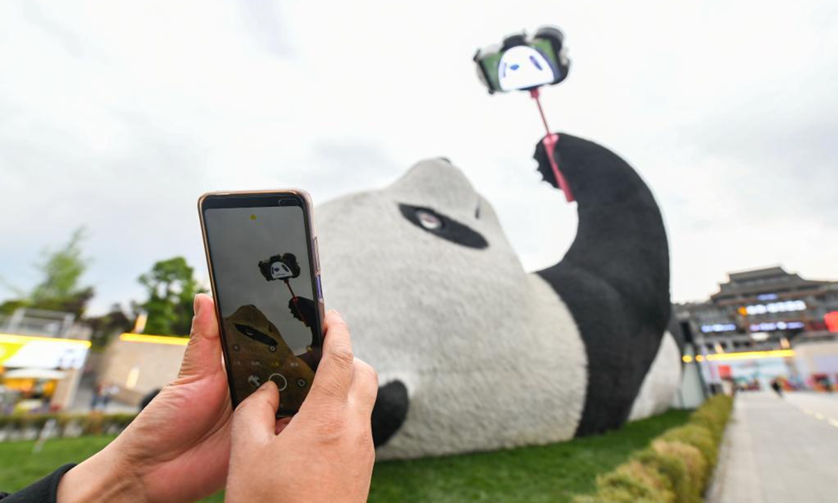 A tourist takes photos of the Selfie Panda sculpture at Yangtianwo square in Dujiangyan, southwest China's Sichuan Province, April 7, 2021.(Xinhua/Wang Xi)