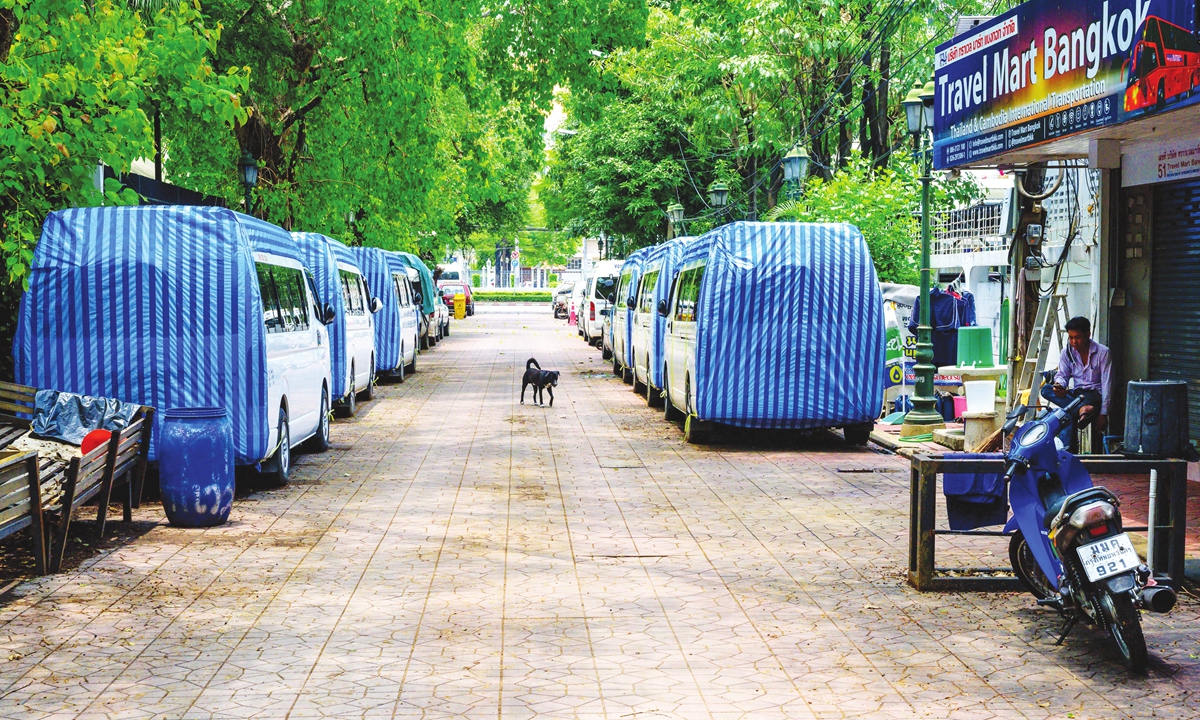 A travel agency employee sits in front of his closed shop while covered vans for tourist transport are parked along an alley in Bangkok, Thailand, on Thursday. The country is considering closing entertainment venues in Bangkok and 40 provinces for the coming Song Kran holiday. Photo: AFP