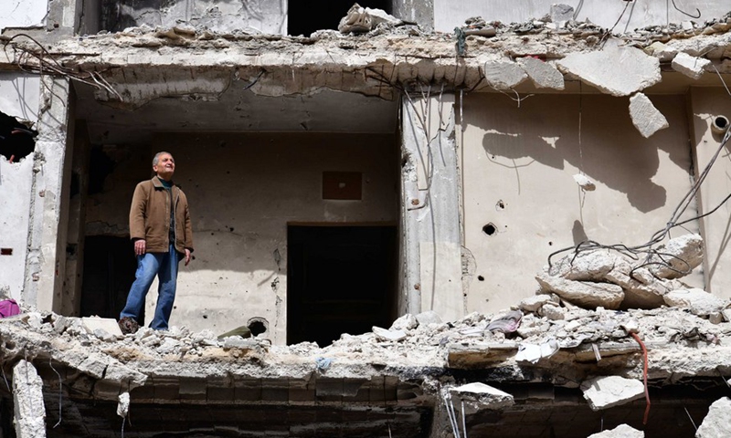 Hadi Ghusoun, a retired English teacher in his late 60s, stands on the porch of his shattered house in Homs city in central Syria, March 11, 2021. (Photo by Ammar Safarjalani/Xinhua)