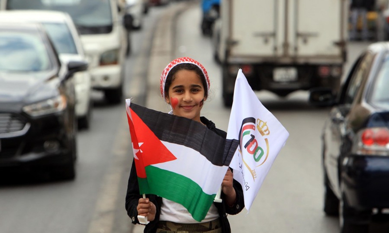 A girl holds a Jordanian national flag and a centenary flag on a street in Amman, Jordan, on April 11, 2021. (Photo: Xinhua)