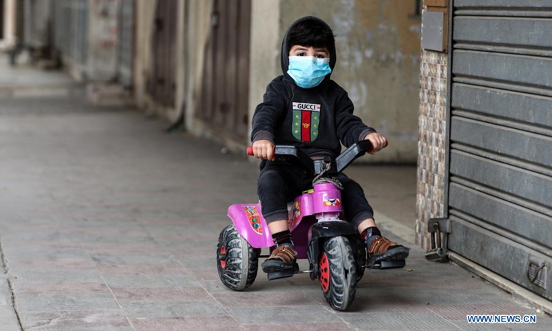 A Palestinian child wearing a face mask plays at an empty street in the southern Gaza Strip city of Khan Younis, April 10, 2021, amid strict measures imposed by the Hamas-run local authorities to curb the COVID-19 pandemic.(Photo: Xinhua)