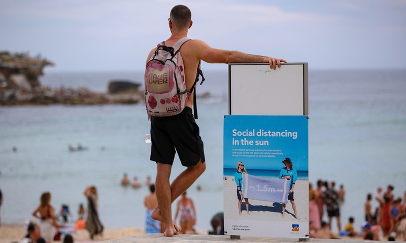 A man stands beside a social distancing notice board at Bondi beach in Sydney, Australia, on Jan. 26, 2021.(Photo: Xinhua)