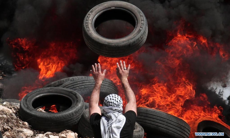A Palestinian protester throws a car tire into fire during clashes after a protest against the expansion of Jewish settlements in Kufr Qadoom village near the West Bank city of Nablus, on April 16, 2021.(Photo: Xinhua)