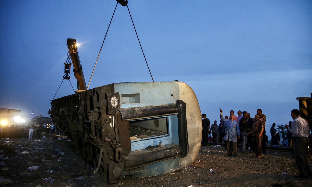 People stand by as a telescopic railway crane lifts an overturned passenger carriage, at the scene of a railway accident in the city of Toukh in Egypt's central Nile Delta province of Qalyubiya on Sunday. The train accident north of Cairo on Sunday left 11 people dead and 98 others injured, after it derailed off its tracks heading northwards from the capital Cairo, the health ministry said, in the latest railway disaster. Photo: AFP
