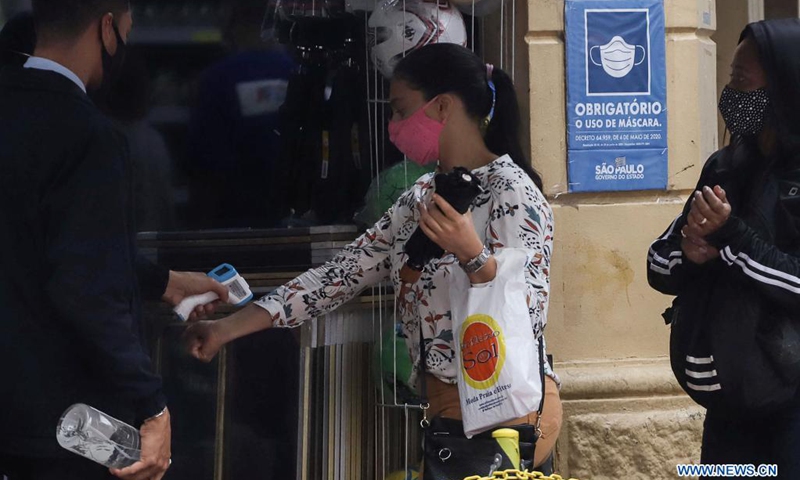 A consumer has her temperature measured at a store entrance on the first business day after commerce closures as a prevention measure against COVID-19 outbreak, in Sao Paulo, Brazil, on April 19, 2021.(Photo: Xinhua)