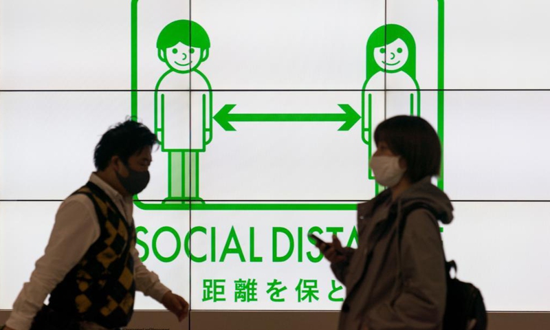 People walk past a social distancing signage in Tokyo, Japan on April 23, 2021. Japan's Prime Minister Yoshihide Suga on Friday declared a third state of emergency over COVID-19 in Tokyo, Osaka, Kyoto and Hyogo. The state of emergency will come into effect from Sunday to May 11.Photo:Xinhua