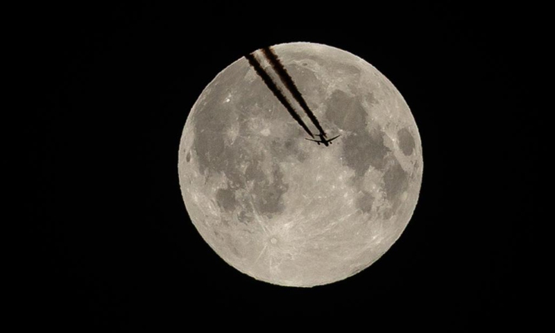 A plane flies against the backdrop of the full moon, also known as the supermoon, in Paris, capital of France, April 27, 2021. (Photo by Aurelien Morissard/Xinhua) 