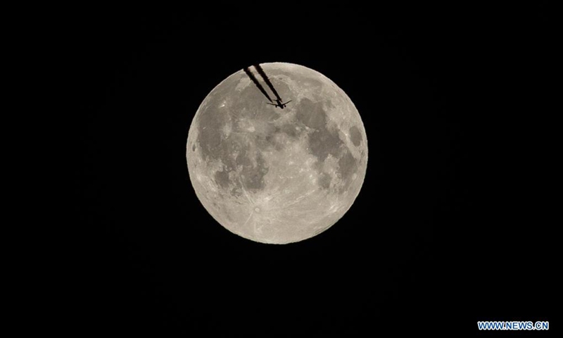 A plane flies against the backdrop of the full moon, also known as the supermoon, in Paris, capital of France, April 27, 2021. (Photo by Aurelien Morissard/Xinhua) 