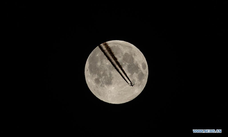 A plane flies against the backdrop of the full moon, also known as the supermoon, in Paris, capital of France, April 27, 2021. (Photo by Aurelien Morissard/Xinhua) 