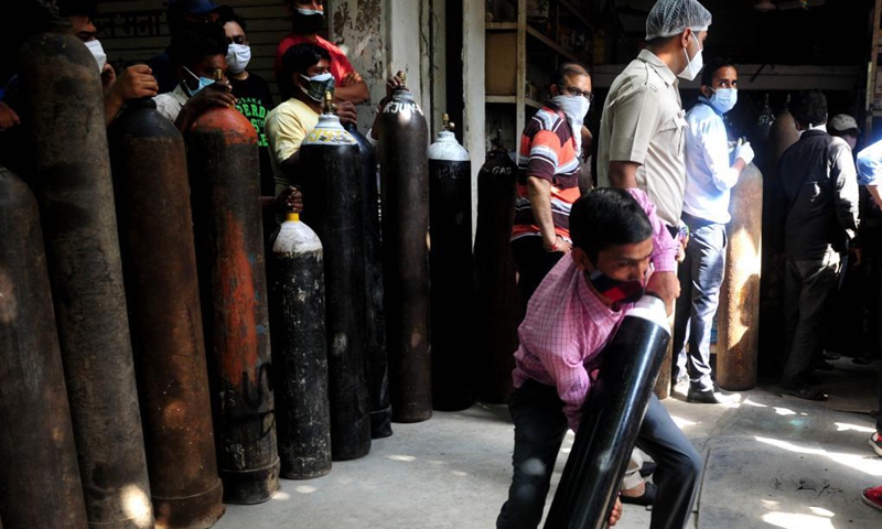 A man lifts a refilled medical oxygen cylinder for COVID-19 patients in front of a shop in New Delhi, India, April 26, 2021. (Photo: Xinhua)