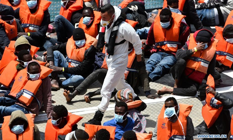 A detention officer walks past migrants wearing face masks upon their arrival in Senglea, south of Malta, on May 11, 2021. A group of around 70 migrants were brought to Malta after being rescued in south of the island during Monday night following a distress call, a spokesperson from the Ministry for Home Affairs, National Security and Law Enforcement, said on Tuesday.(Photo: Xinhua)