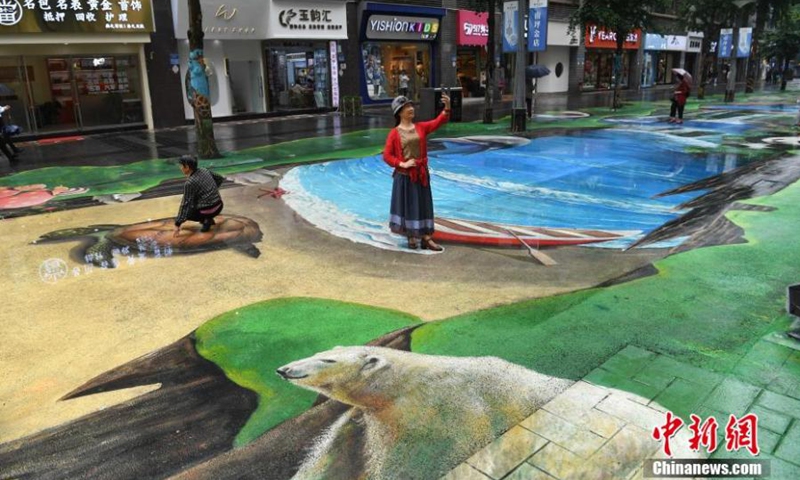 A woman takes a selfie featured with a naked eye 3D pavement painting featuring nature and ecoloy in Chongqing, May 12, 2021.Photo:China News Service