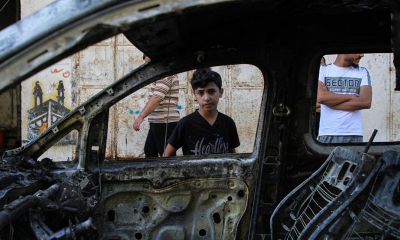 Palestinian boy Mohammad Nasr, 7 years old, poses for a photo near a car which was hit by an Israeli air strike near his house in Gaza City, on May 19, 2021.(Photo: Xinhua)