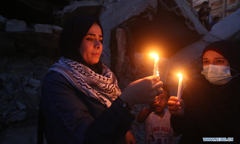 Palestinians hold candles near buildings destroyed in Israeli air strikes in the southern Gaza Strip city of Rafah, on May 25, 2021. Limited international relief cargo, COVID-19 vaccines and aid workers are allowed into Gaza while the United Nations calls on Israel to open all crossings, UN humanitarians said on Tuesday.(Photo: Xinhua)