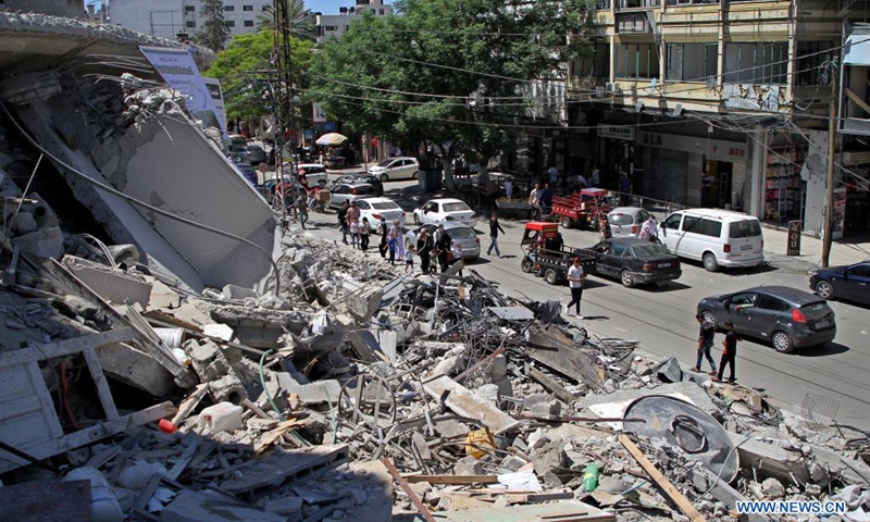 Palestinians walk past the rubble of Al-Shorouq Tower destroyed during an Israeli air strike in Gaza City, May 23, 2021.(Photo: Xinhua)