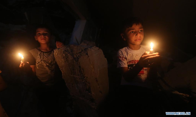 Palestinian children hold candles near buildings destroyed in Israeli air strikes in the southern Gaza Strip city of Rafah, on May 25, 2021. Limited international relief cargo, COVID-19 vaccines and aid workers are allowed into Gaza while the United Nations calls on Israel to open all crossings, UN humanitarians said on Tuesday.(Photo: Xinhua)
