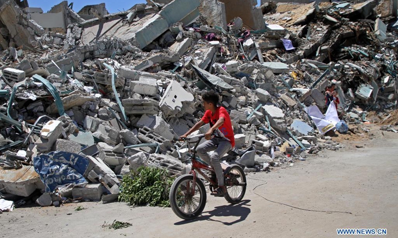 A Palestinian boy rides his bicycle past the rubble of Jala Tower destroyed during an Israeli air strike in Gaza City, May 23, 2021.(Photo: Xinhua)