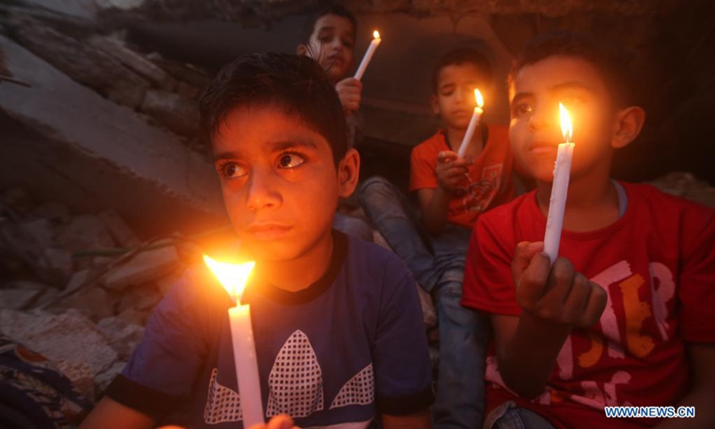 Palestinian children hold candles near buildings destroyed in Israeli air strikes in the southern Gaza Strip city of Rafah, on May 25, 2021. Limited international relief cargo, COVID-19 vaccines and aid workers are allowed into Gaza while the United Nations calls on Israel to open all crossings, UN humanitarians said on Tuesday.(Photo: Xinhua)