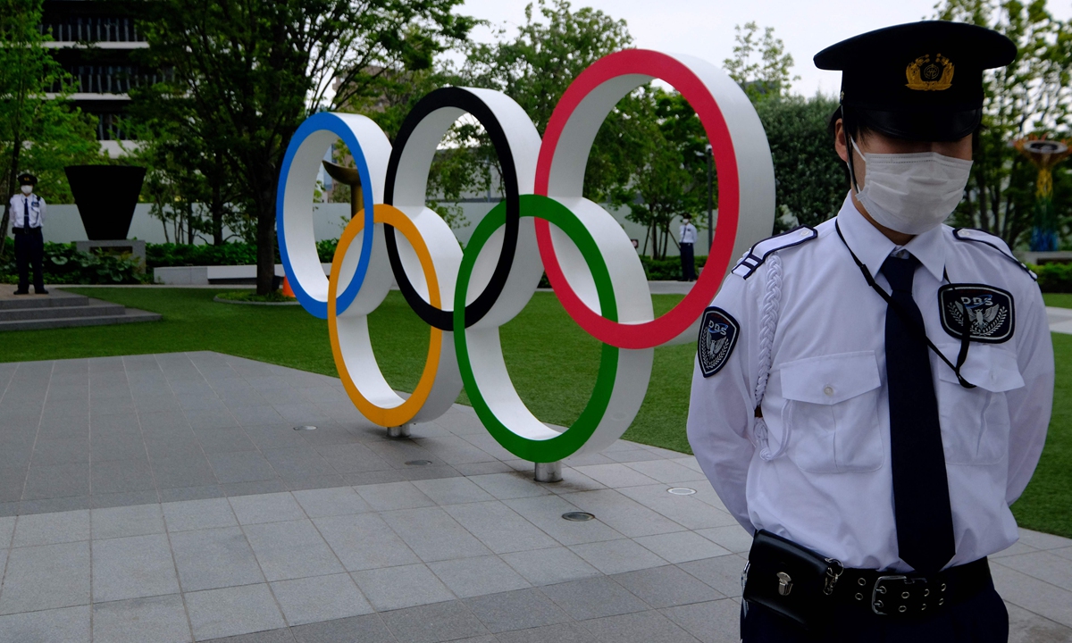Security guards keep watch next to the Olympic Rings while people take part in a protest against the hosting of the 2020 Tokyo Olympic Games, in front of the headquarters building of the Japanese Olympic Committee in Tokyo, on May 18, 2021. Photo: VCG
