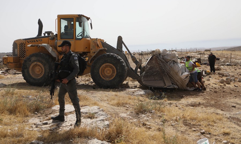 Laborers work on confiscation of a tent as a member of border police stand guard in Zif village, south of the West Bank city of Hebron, on May 31, 2021.(Photo: Xinhua)