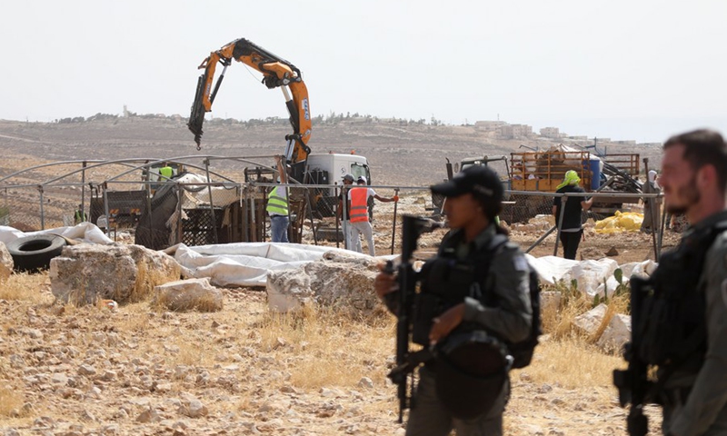 Laborers work on confiscation of a tent as members of border police stand guard in Zif village, south of the West Bank city of Hebron, on May 31, 2021.(Photo: Xinhua)