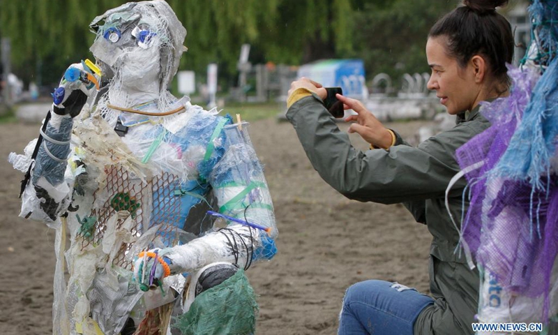 A woman takes photos of a figure made with plastics removed from shorelines at Kitsilano Beach in Vancouver, British Columbia, Canada, on June 6, 2021. Created by multidisciplinary artist Caitlin Doherty and made with plastics removed from Canadian shorelines, a set of figures named plastic beachgoers embody people's collective contribution to plastic pollution, bring the topic of shoreline pollution to the forefront.(Photo: Xinhua)