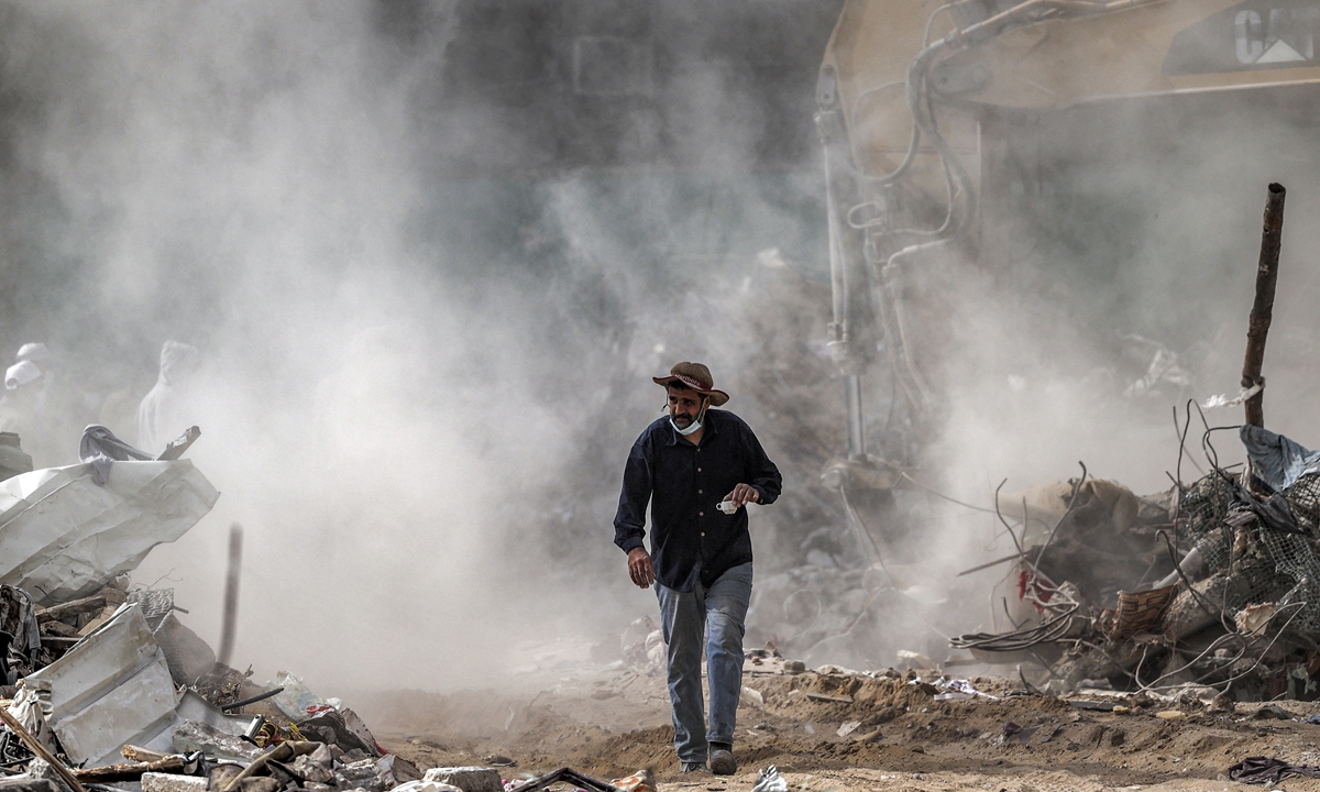 A Palestinian man walks with a cup of coffee past a cloud of dust from the demolition of a building destroyed during the May 2021 conflict between Hamas and Israel, in Gaza City on Saturday. Photo: AFP