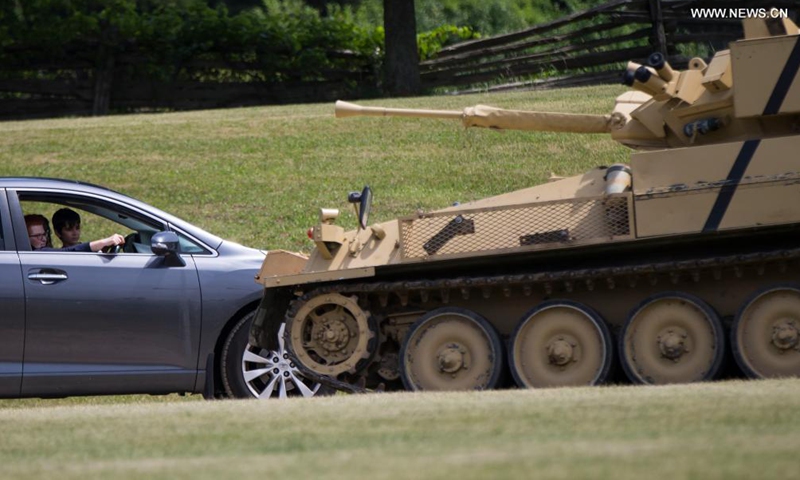 People look at a military vehicle from their car at the 2021 Mega Wheels Drive-Thru event in Milton, Ontario, Canada, on June 20, 2021. The drive-thru event, held from June 18 to 27, features monster trucks, classic cars, military vehicles and more through a 2.5 km course.(Photo: Xinhua)