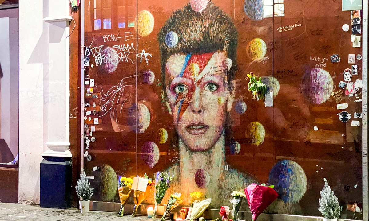 Flowers and candle lie before a mural depicting the cover of Aladdin Sane in London on January 10 to remember the firth anniversary of the death of David Bowie. Photo: AFP