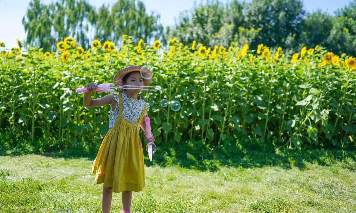 A girl blows bubbles near sunflowers at the Beijing Olympic Forest Park in Beijing, capital of China, July 4, 2021. (Xinhua/Chen Yehua)