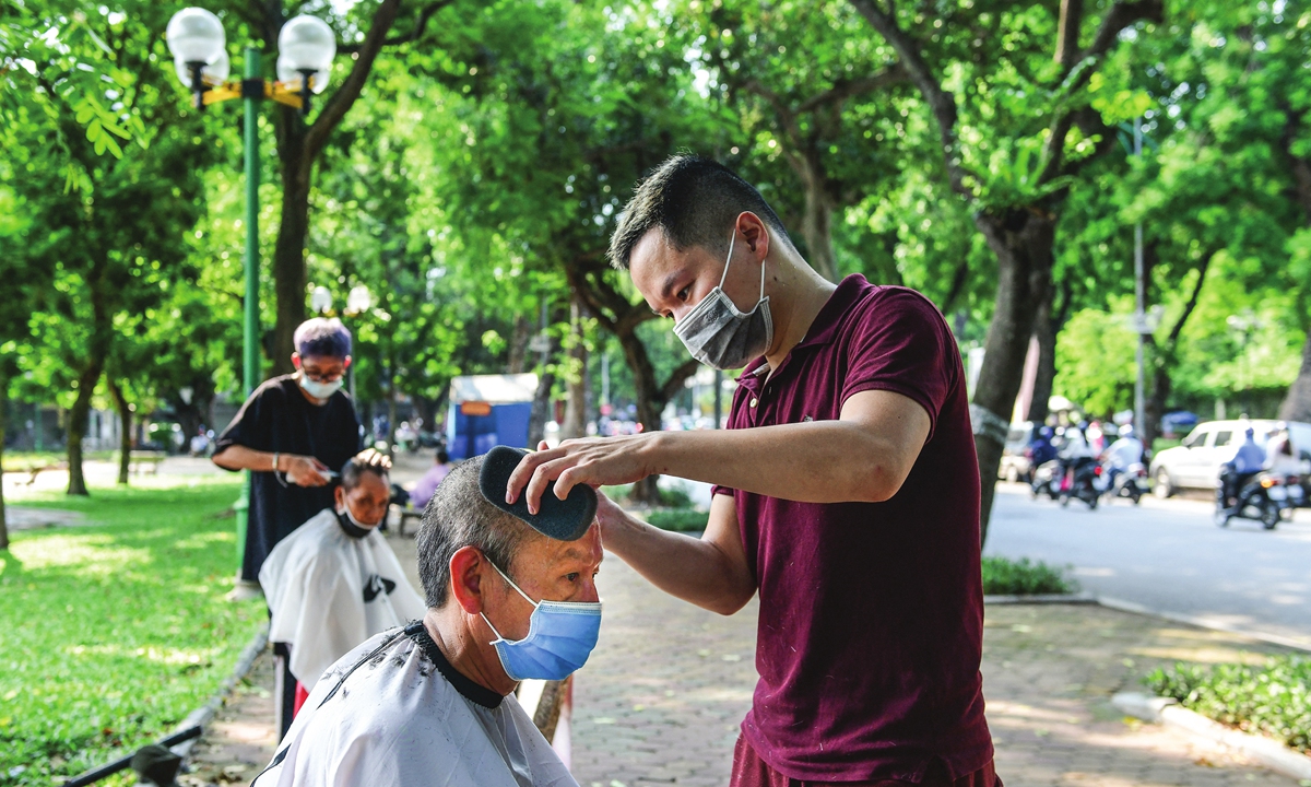 Roadside barbers cut customers' hair in Hanoi, Vietnam, on Tuesday. Hanoi had reported two new outbreaks of COVID-19 on Tuesday morning, with 10 people infected after the capital went 10 days without any new cases in the community. The Ministry of Health has confirmed a total of 19,933 cases of COVID-19 in the country. Photo: AFP