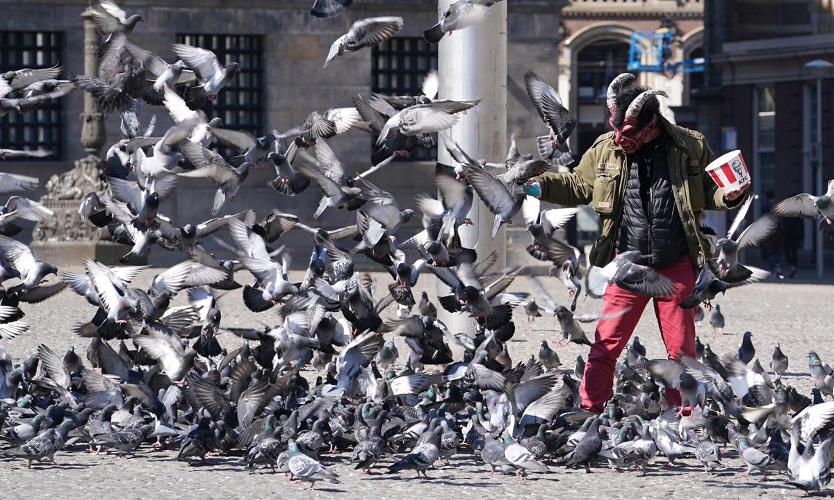 A man wearing a mask is feeding pigeons on Dam Square in Amsterdam on April 5, 2020. Photo: VCG