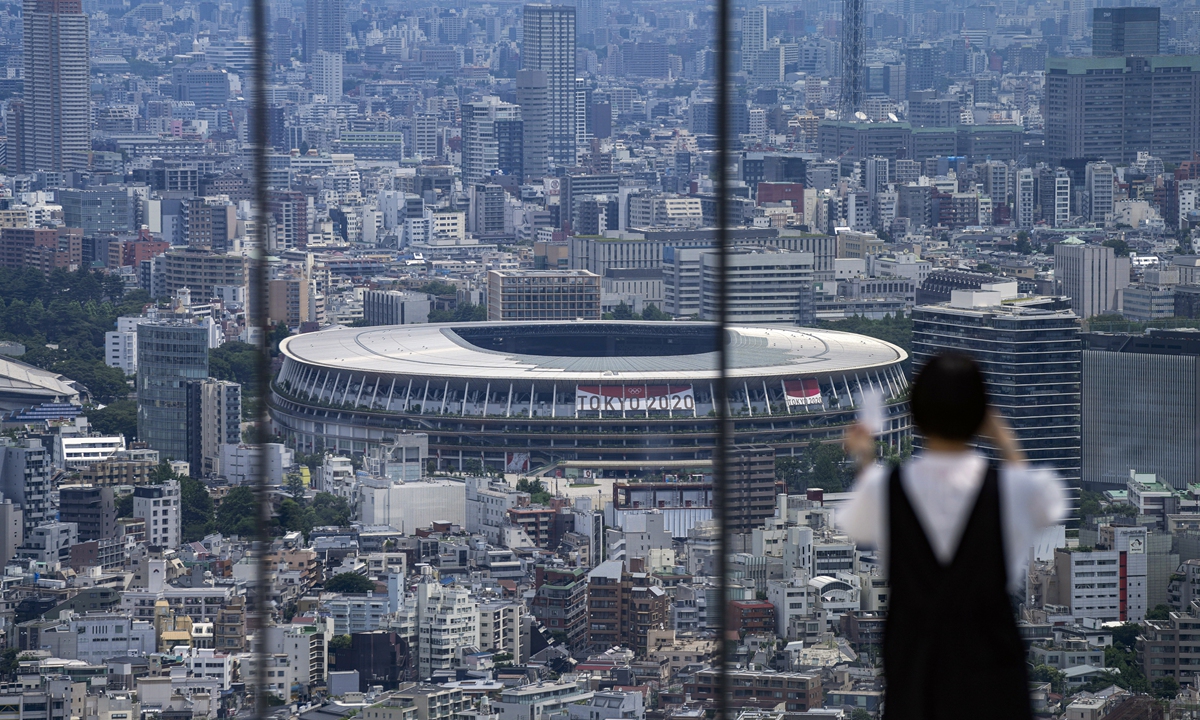 A resident wearing a protective mask takes a picture from an observation deck as the National Stadium, where the opening ceremony of the Tokyo 2020 Olympics will be held in less than two weeks, is seen in the background on Saturday in Tokyo, Japan. Photo: VCG