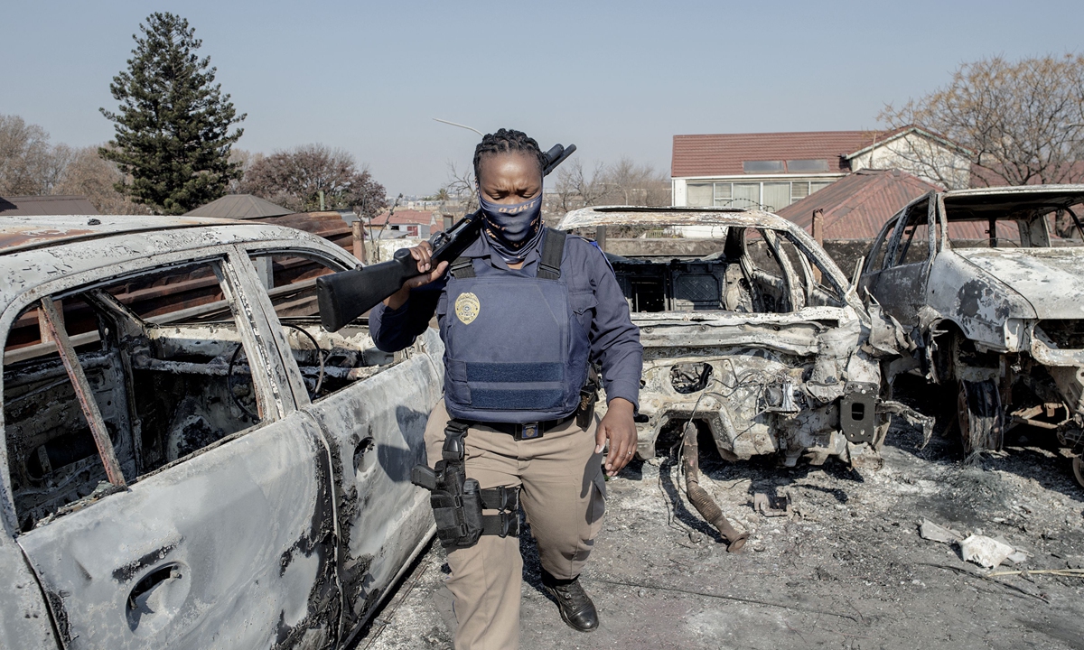A Johannesburg Metro Police Department officer walks between burnt cars at a car showroom in Johannesburg on Sunday. Several shops are damaged and cars burnt in Johannesburg, following a night of violence. Photo: VCG