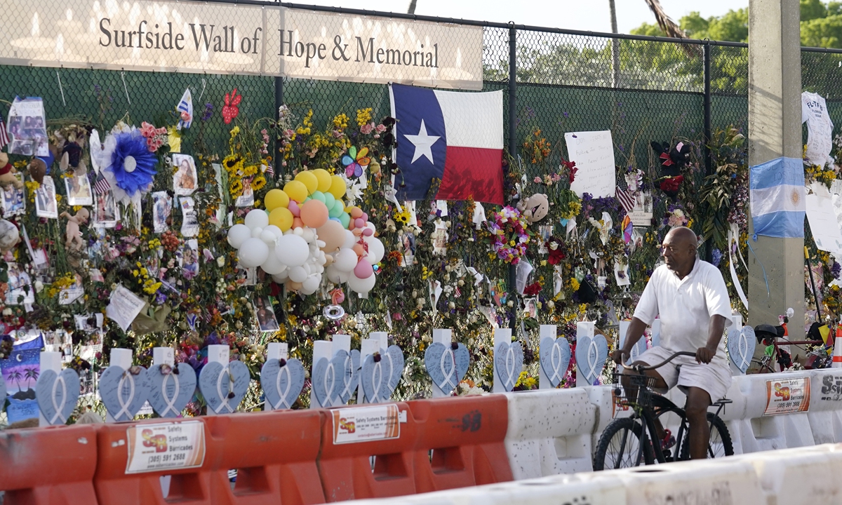 A cyclist rides past a makeshift memorial recognizing the victims of the partially collapsed Champlain Towers South building, as removal and recovery work continues at the site in Surfside, Florida on Tuesday. Photo: VCG