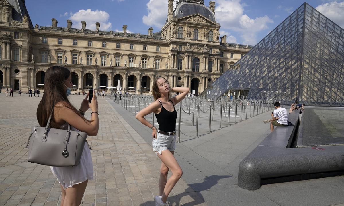 A tourist poses for a photo by her friend outside the Louvre Museum in Paris on June 9. Photo: VCG