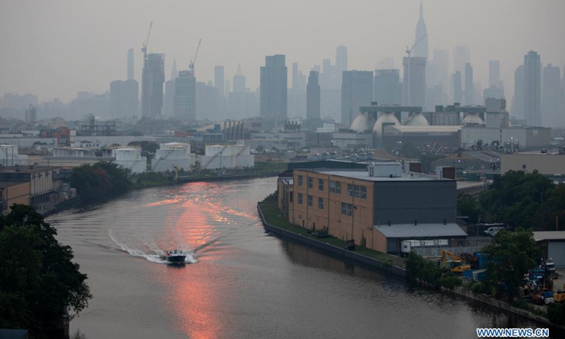 A boat moves in sunlight reflections on a river as the Manhattan skyline is surrounded in a thick haze in New York, the United State, July 20, 2021. Smoke from the wildfires in the western U.S. has contributed to the haze, according to local weather service. (Xinhua)