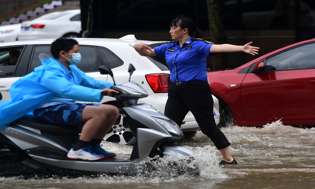 A government employee in Zhengzhou guides traffic through a waterlogged section of Huangyuan Road on Wednesday. Photo: VCG