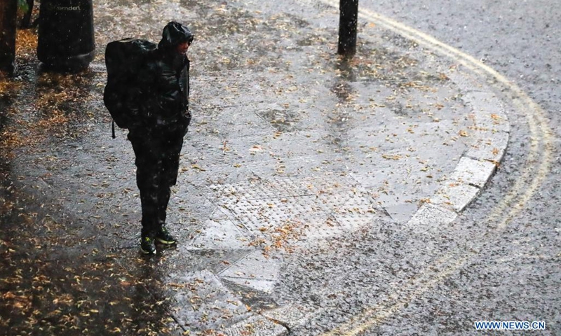 A man stands on the roadside during a heavy rain in London, Britain, on July 25, 2021. Heavy downpours and thunderstorms have caused severe flash flooding in parts of London on Sunday, according to local media(Photo: Xinhua)